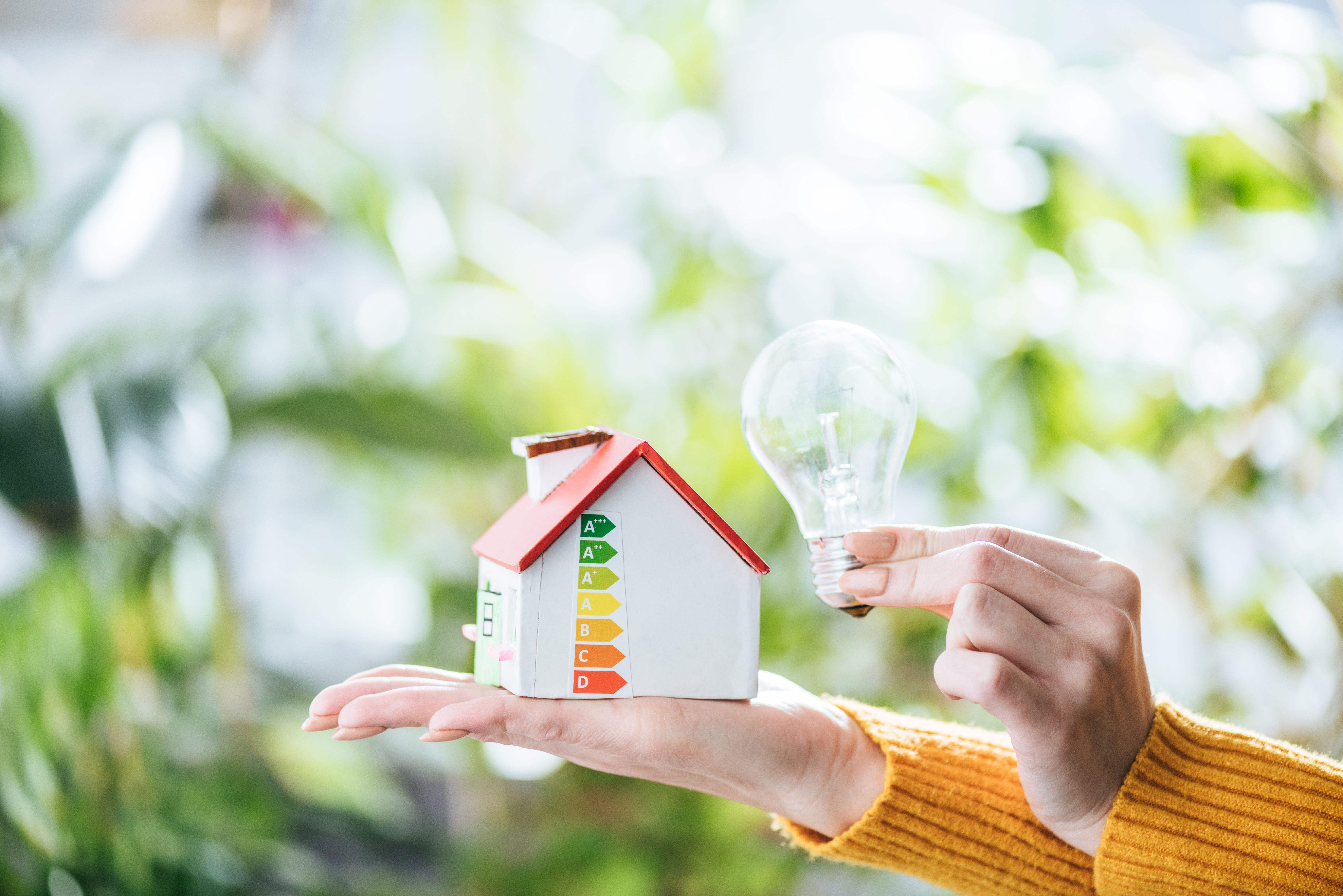 Mujer sosteniendo una bombilla LED y una maqueta de vivienda